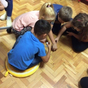 pokaż obrazek - Grupa dzieci siedząca na podłodze. Z wylosowanych kostek z postaciami bajkowymi starają się ułożyć opowieść.