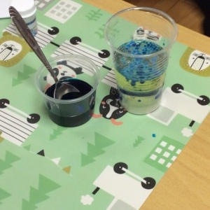pokaż obrazek - Na stoliku stoją dwa pojemniki. W jednym granatowy barwnik i łyżeczka a w drugim olej z niebieskimi bąbelkami.